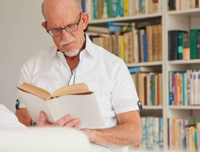 Homme senior lisant un livre devant une bibliothèque